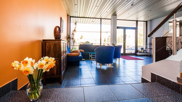 A modern lobby with a wooden ceiling, a vase of flowers, and a seating area with blue chairs. - Kert (Riga)