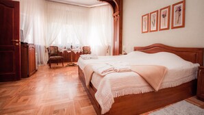 A bedroom with a wooden bed, a chair, a desk, and a window with sheer curtains. - Kert (Riga)