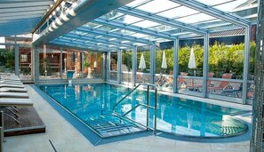 A swimming pool with a glass ceiling, lounge chairs, and umbrellas. - Wellness Landhotel Prinz Wellness Romantik (Anger)