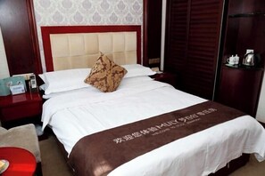 A hotel room with a bed, a nightstand, a red chair, a wardrobe, and a small table with a kettle. - Nongken Hotel (Lanzhou)