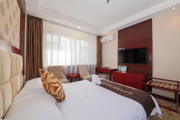 A hotel room with a large bed, a TV, a desk, and a chair.