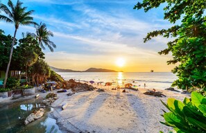 A beach with a sunset, palm trees, and umbrellas. - Silver Resortel (Patong)