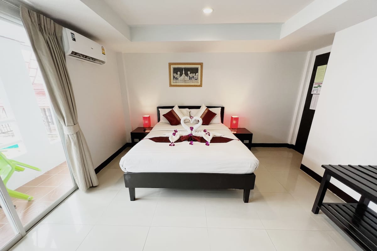 A hotel room with a large bed, two bedside tables with lamps, a picture on the wall, and a bench by the window.