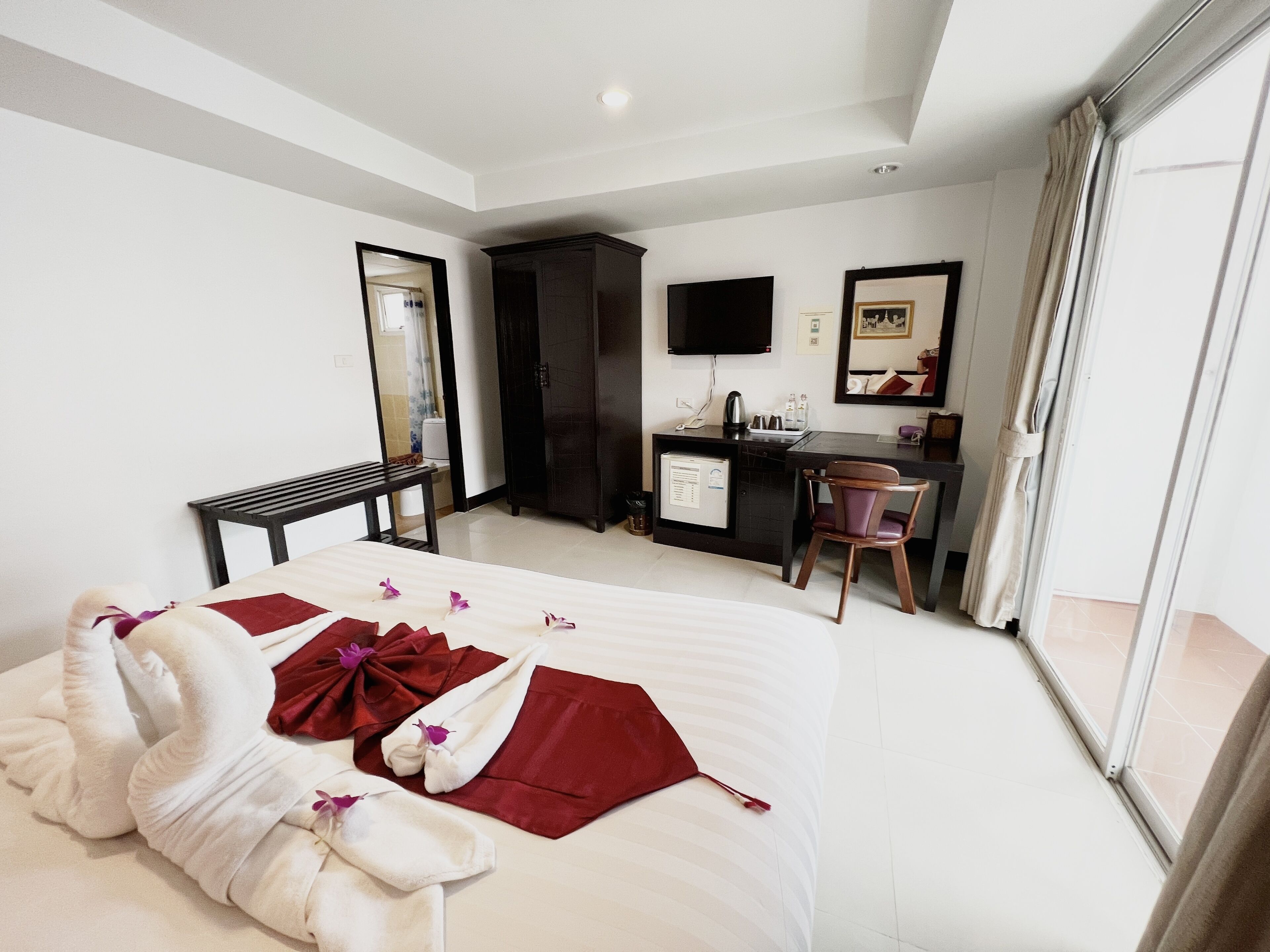 Habitación de hotel con cama, escritorio, silla, armario, televisor de pantalla plana y ventana grande.
