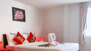 A neatly made bed with white linens and red pillows, a wall-mounted painting, and a window with curtains. - Silver Resortel (Patong)