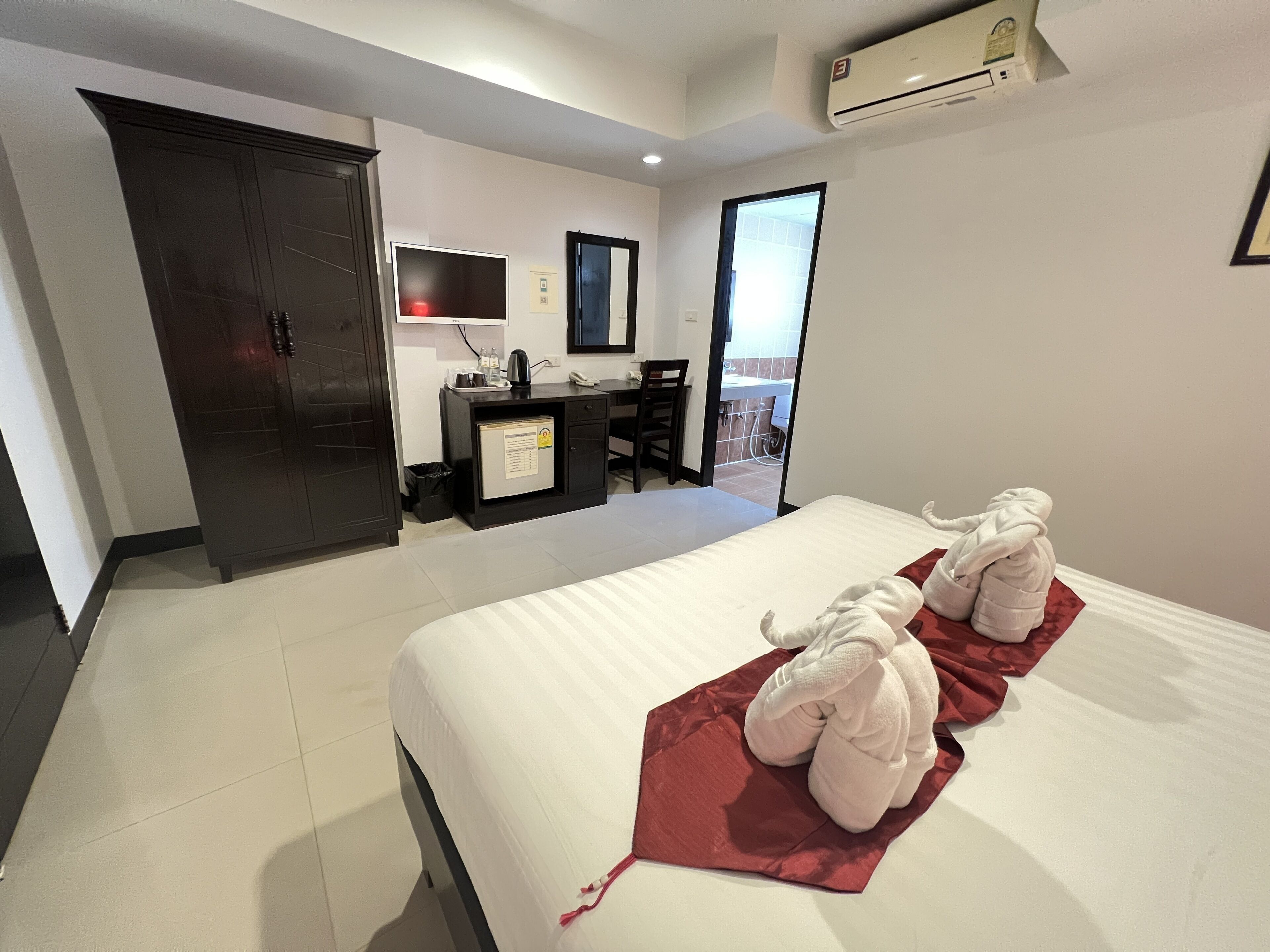 Una camera d'albergo con un letto, una scrivania, una sedia, un armadio e un condizionatore d'aria.