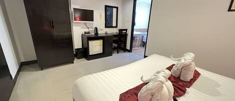A hotel room with a bed, a desk, a chair, a wardrobe, and an air conditioning unit.