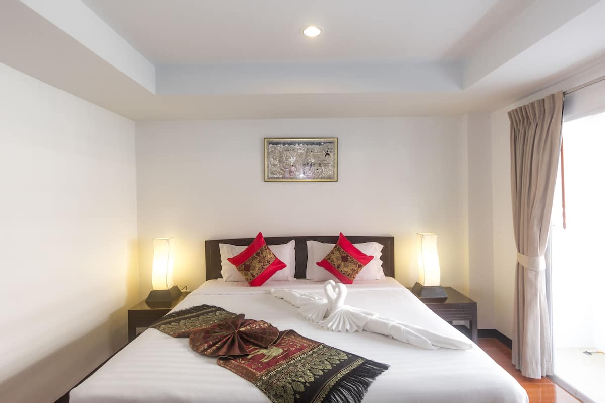 A hotel room with a neatly made bed, two bedside lamps, a framed artwork on the wall, and a window with curtains.