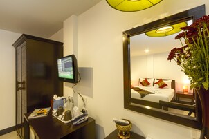 Habitación de hotel con televisión, espejo, escritorio con control remoto y un florero con flores.