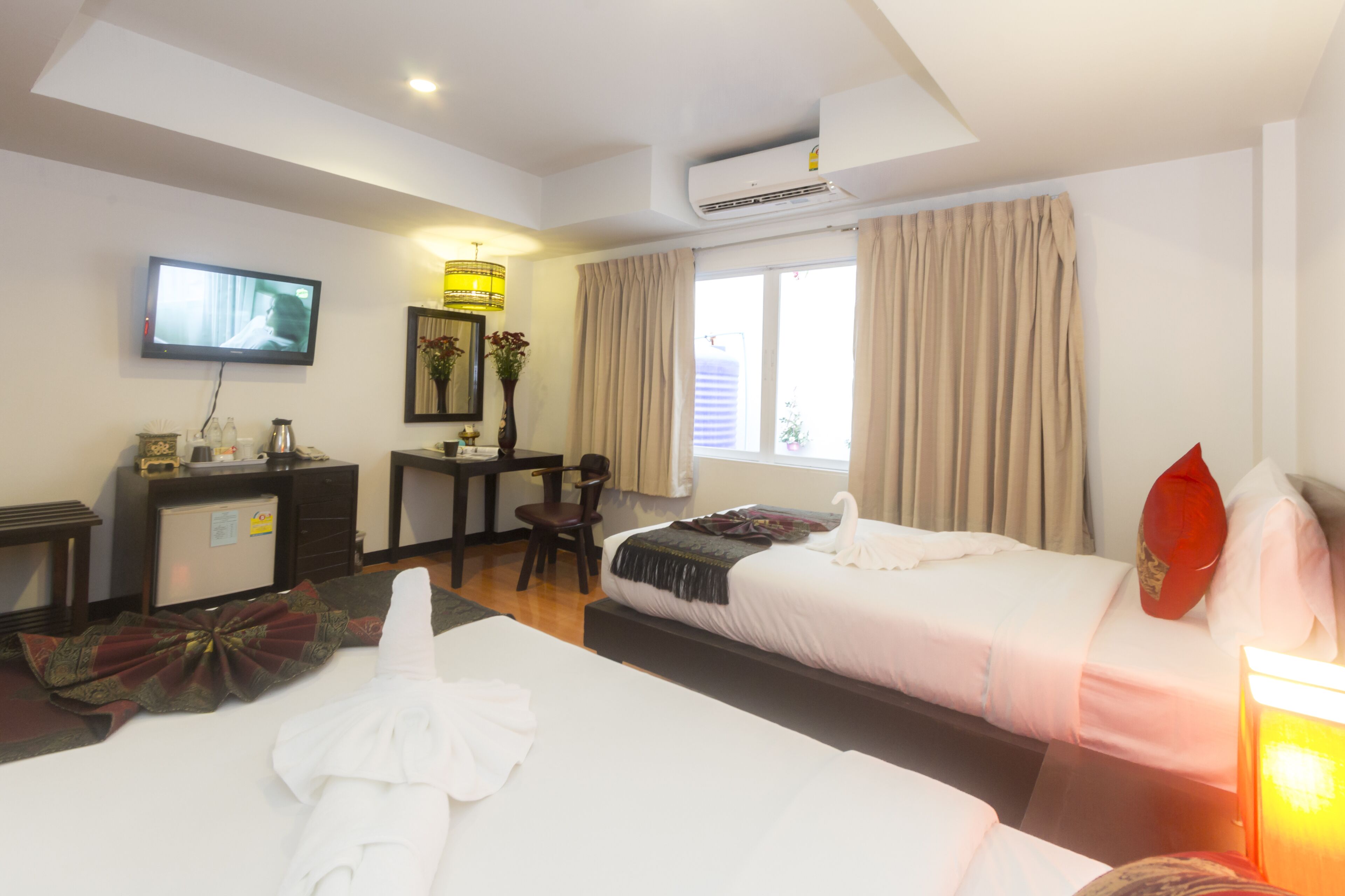 A hotel room with two beds, a desk, a television, and a window with curtains.