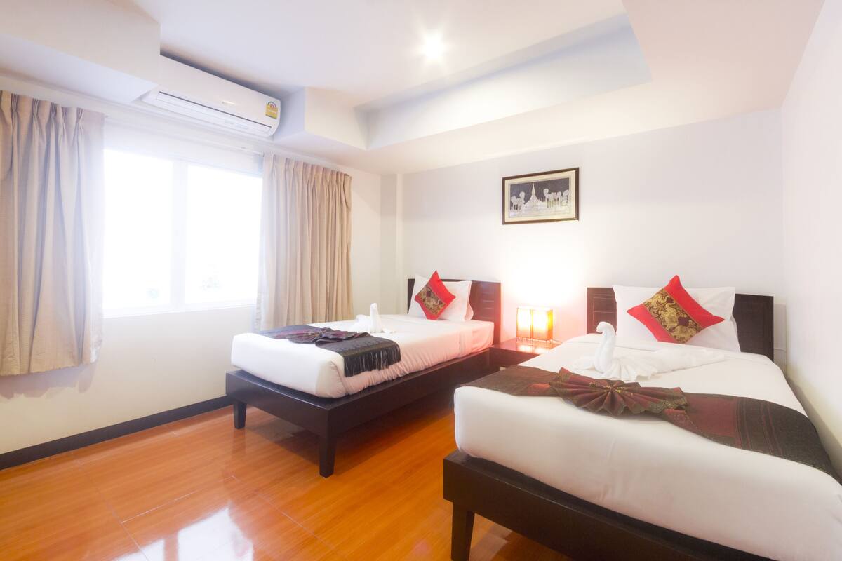 A hotel room with two beds, a large window with curtains, an air conditioning unit, and a framed picture on the wall.