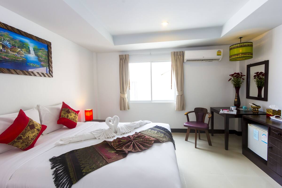 A hotel room with a bed, a desk, a chair, a small refrigerator, and a window with curtains.
