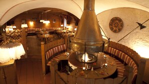 A rustic interior with wooden furniture, a central fire pit, and a vaulted ceiling.
