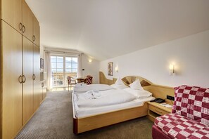 A hotel room with a large bed, a wooden wardrobe, a desk with a chair, and a balcony with a view. - Ruster Resort (Lagundo)