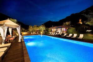 A swimming pool with lounge chairs and a covered seating area, surrounded by mountains and a church. - Ruster Resort (Lagundo)