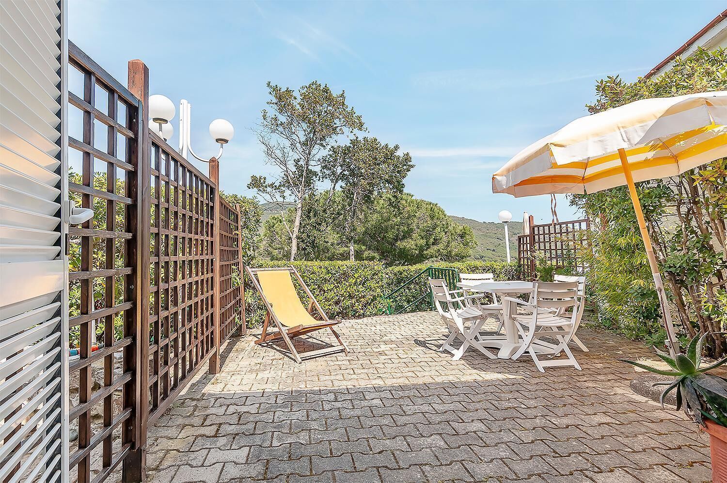 A patio area with a wooden fence, a yellow lounge chair, white outdoor furniture, and a large umbrella.