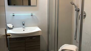 Ein modernes Badezimmer mit einer Glaskabine für die Dusche, einem Waschbecken mit Spiegel darüber und Holzschränken.