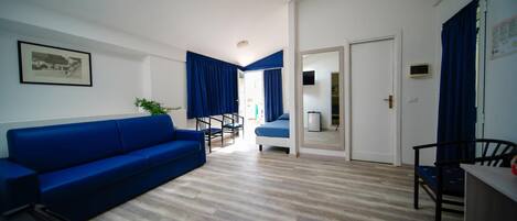 A modern living room with a blue sofa, wooden flooring, and a skylight.