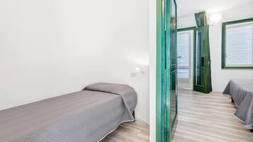 A room with two single beds, a wooden floor, and a green-framed door.