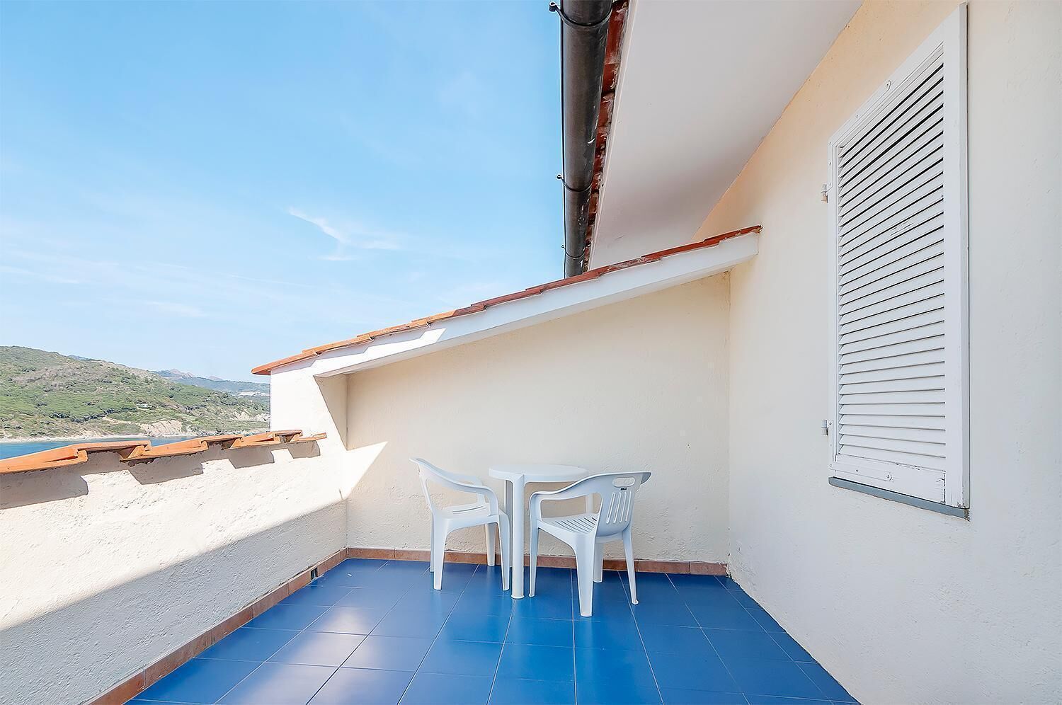 A balcony with a blue floor, white walls, and a white table with two chairs.