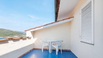 A balcony with a blue floor, white walls, and a white table with two chairs.
