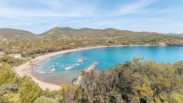 Un paisaje costero con una playa, barcos y colinas al fondo.