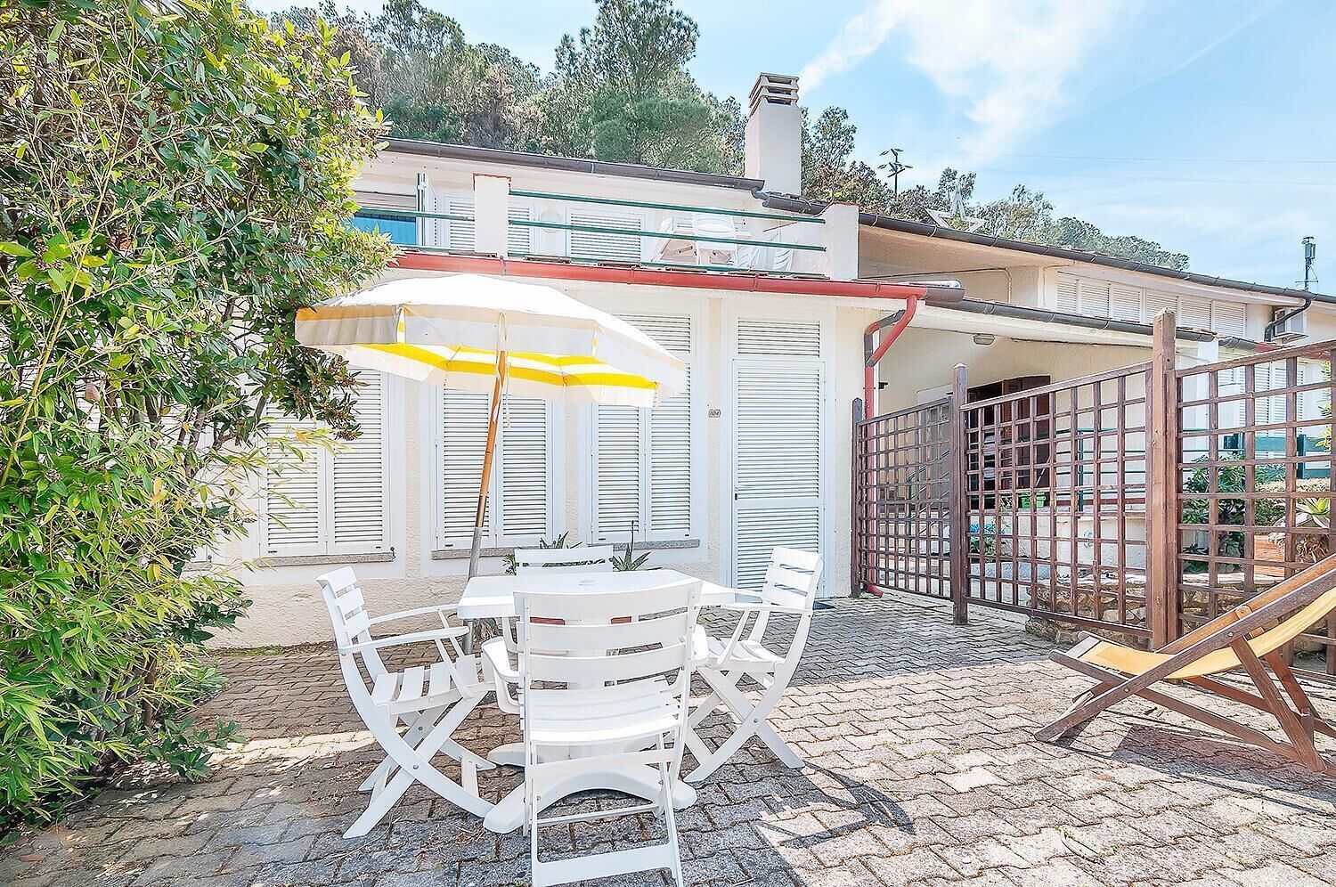An outdoor patio with a white table and chairs, a yellow umbrella, and a gate.