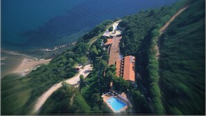 Vista aérea de una propiedad costera con piscina, playa y zona arbolada.