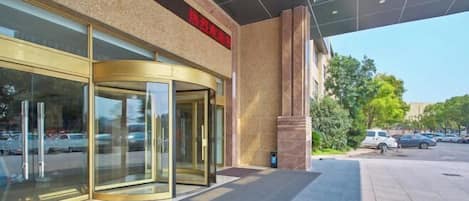 Entrada de hotel con puerta giratoria, fachada de vidrio y vista despejada al estacionamiento.