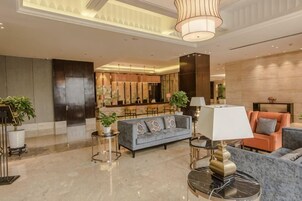 Vestíbulo de hotel con área de descanso, bar y mostrador de recepción.