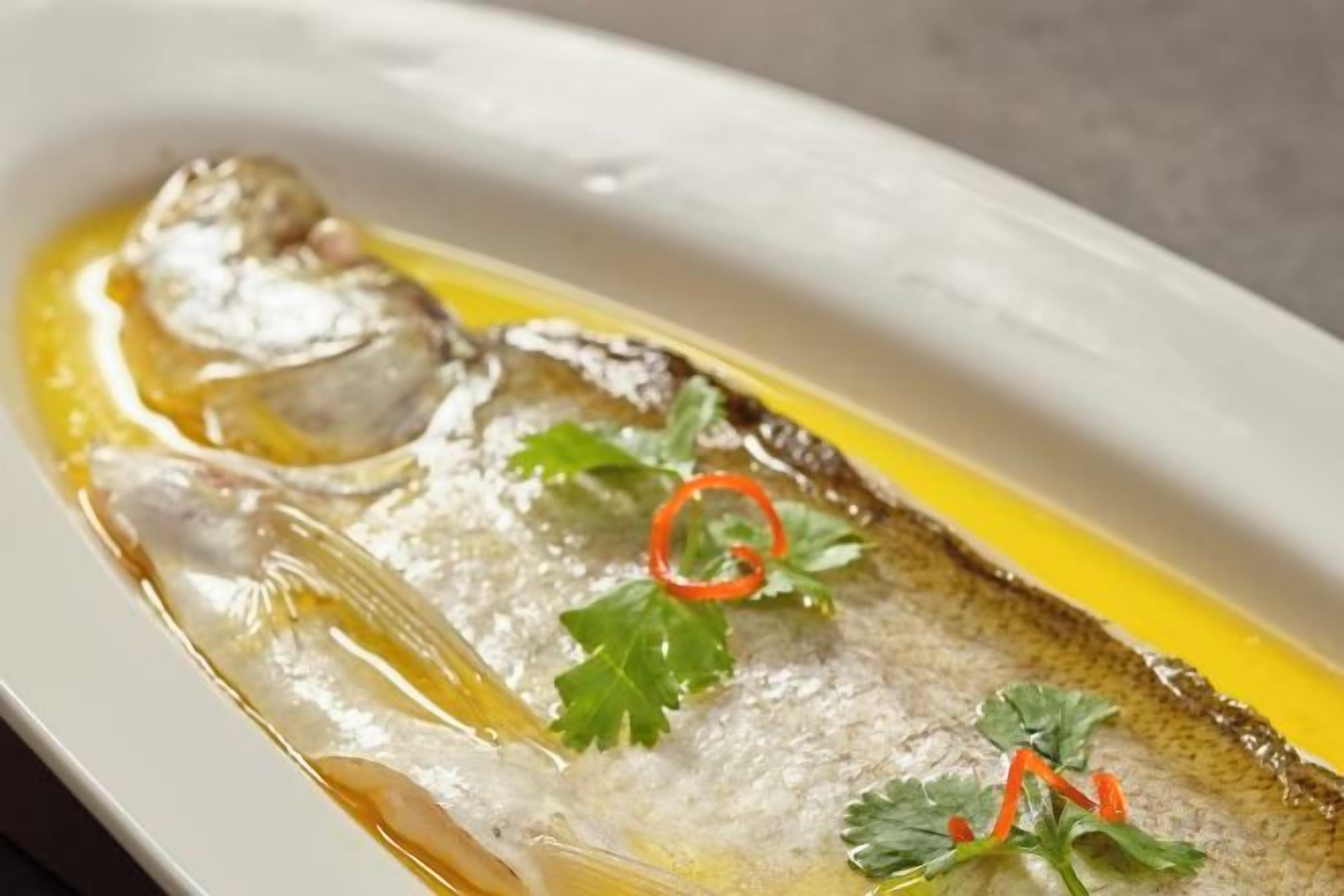 Une assiette ovale blanche, sur laquelle on a disposé un poisson et quelques accompagnements.