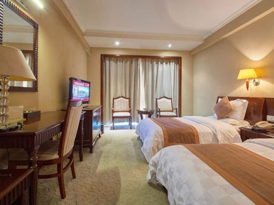 Habitación de hotel con dos camas, un escritorio con silla, un televisor y una lámpara.