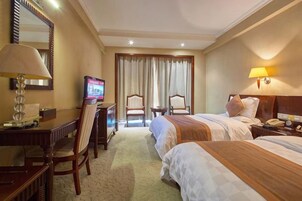 Habitación de hotel con dos camas, un escritorio con silla, un televisor y una lámpara.