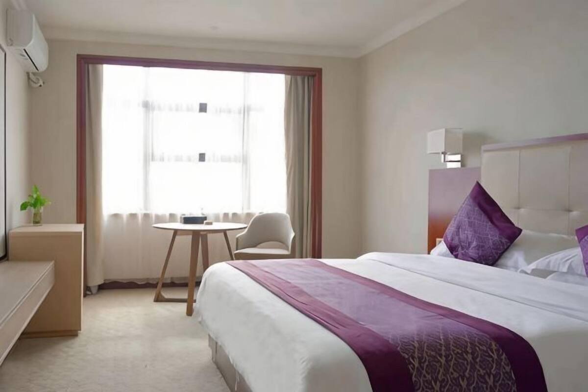Een hotelkamer met een bed, een bureau, een stoel, een klein tafeltje en een raam met gordijnen.