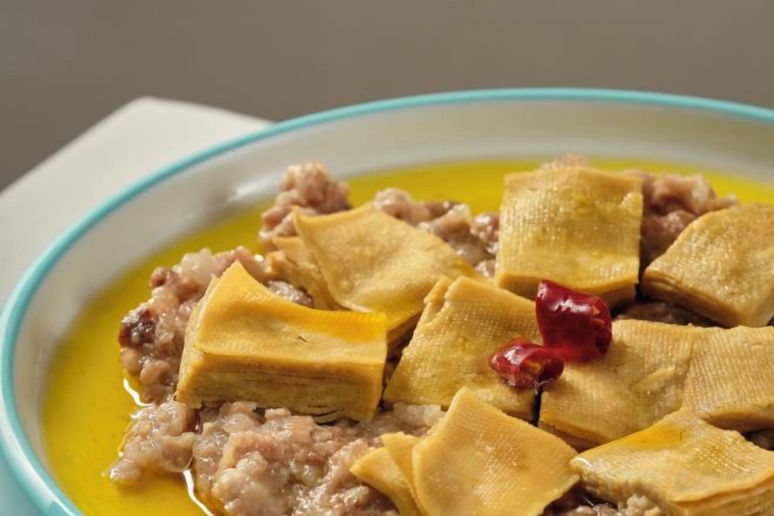 A bowl of food with a yellowish liquid and pieces of food on top.