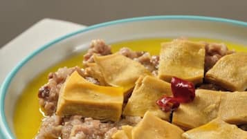A bowl of food with a yellowish liquid and pieces of food on top.