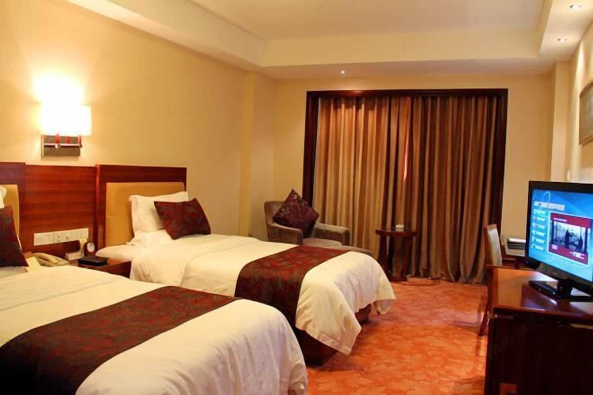 Een hotelkamer met twee bedden, een televisie, een bureau en een stoel.