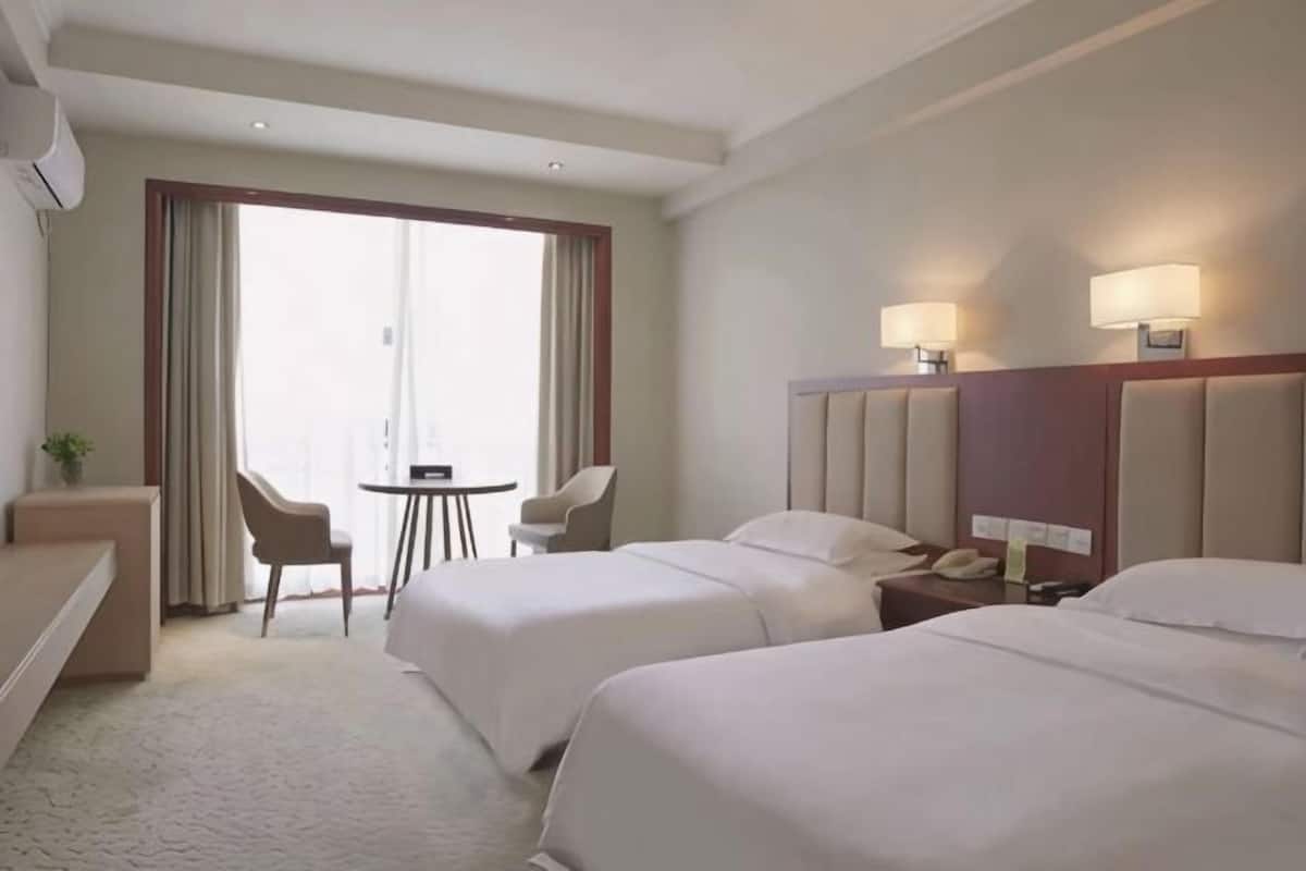 Een hotelkamer met twee bedden, een bureau, een stoel, een kleine tafel en een groot raam.