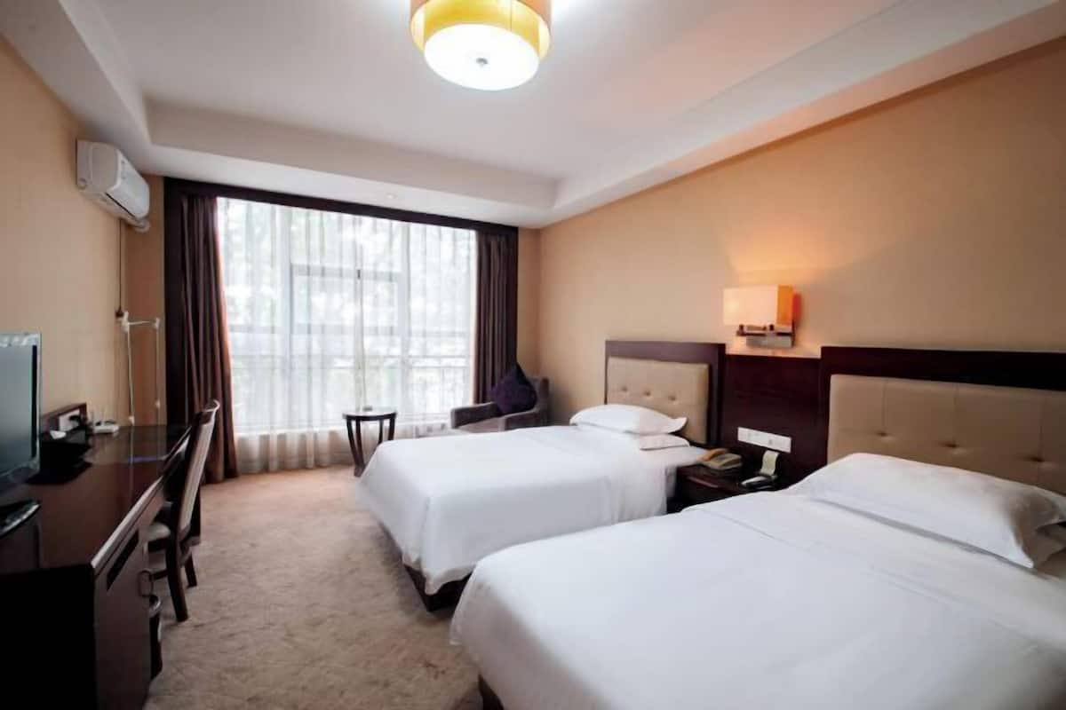 Een hotelkamer met twee bedden, een bureau, een stoel, een televisie en een raam met gordijnen.