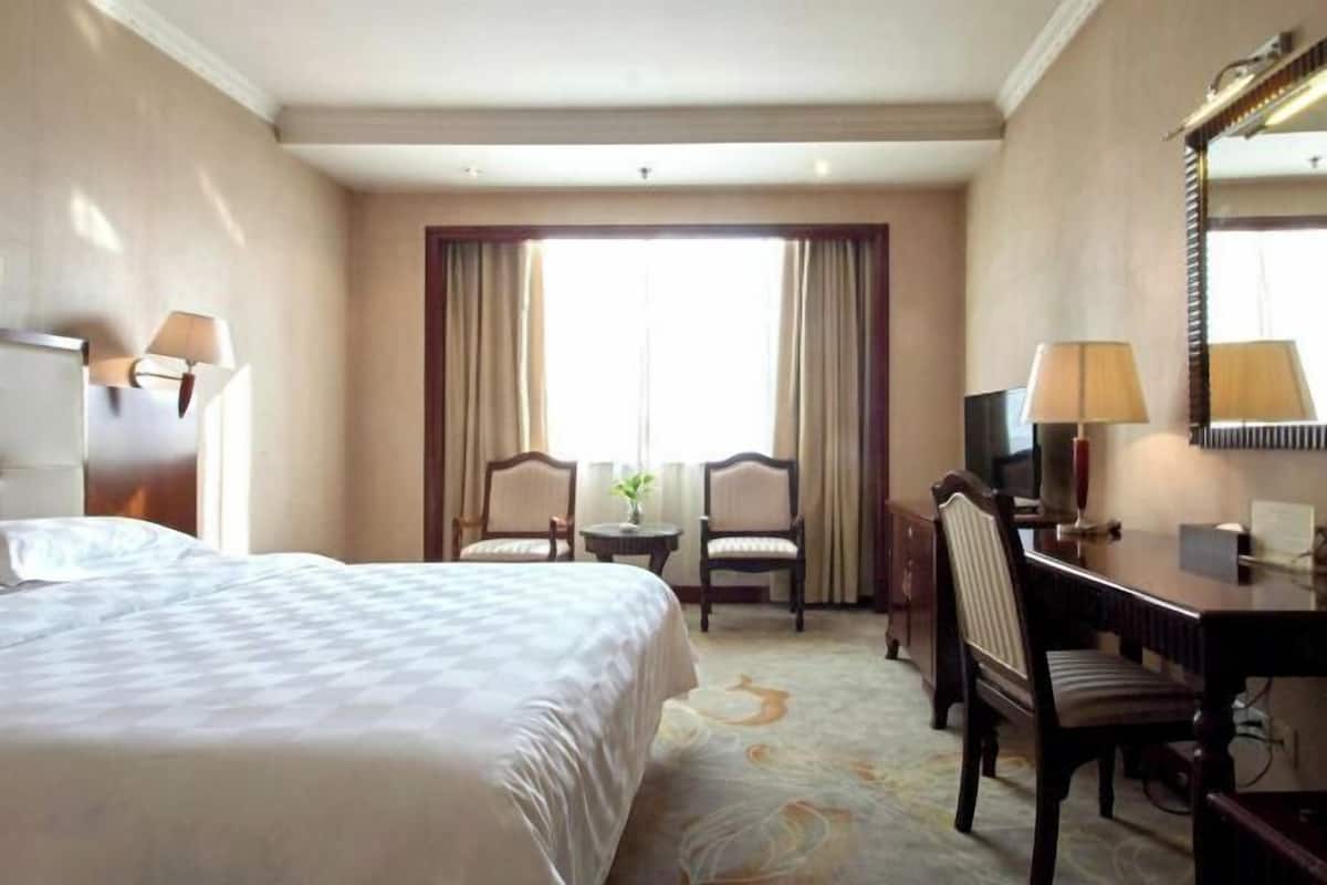 Een hotelkamer met een bed, twee stoelen, een bureau, een televisietoestel en een groot raam met gordijnen.
