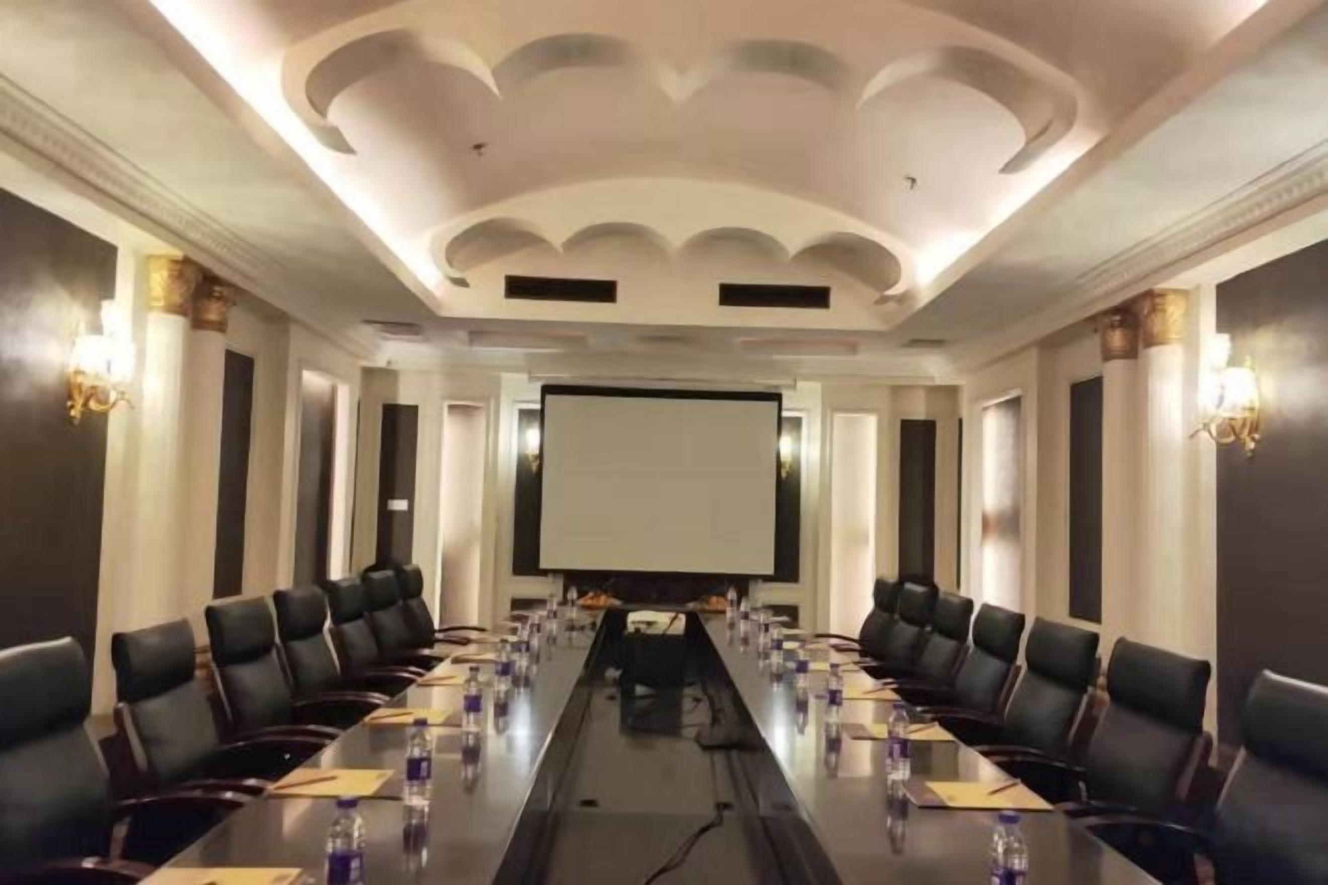 A conference room with a long table, chairs, a projector screen, and a whiteboard.