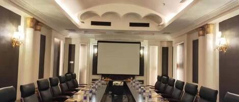 A conference room with a long table, chairs, a projector screen, and a whiteboard.