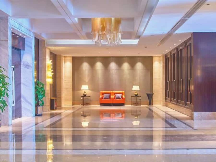 Un vestíbulo de hotel con piso reflectante, una zona de estar con sofá y dos lámparas, y una planta grande a la izquierda.