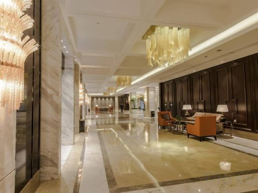 Et hotellobby med marmorgulv, siddeområde med stole og borde, samt en stor lysekrone.