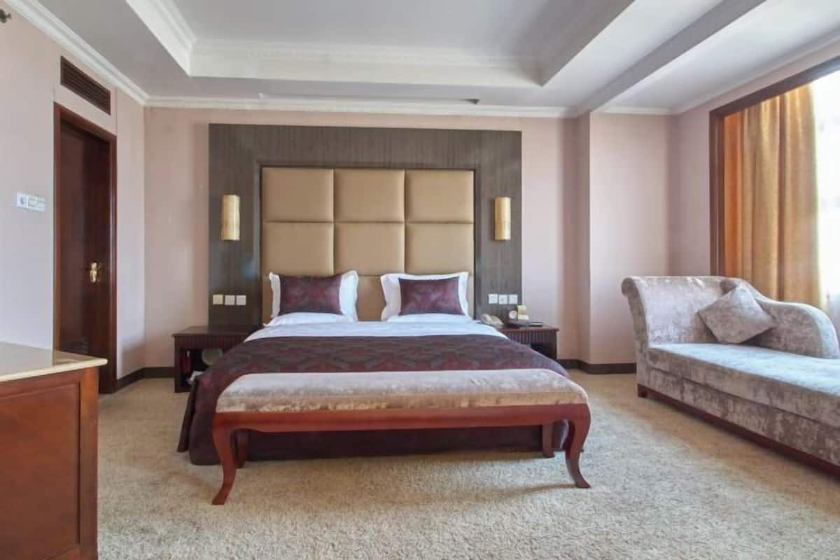 Een hotelkamer met een groot bed, een slaapbank, een houten dressoir en een nachtkastje met een lamp.