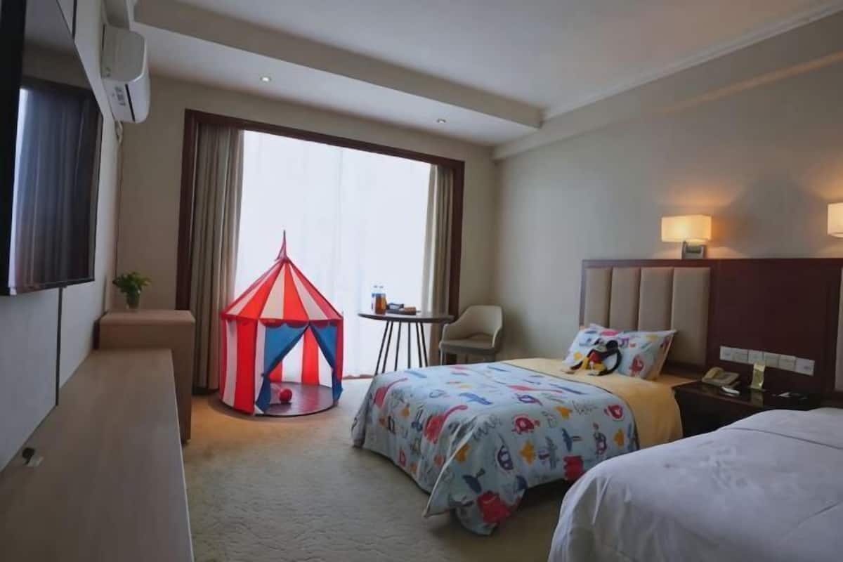 Een hotelkamer met een bed, een tafeltje, een stoel, een televisie en een raam met gordijnen.