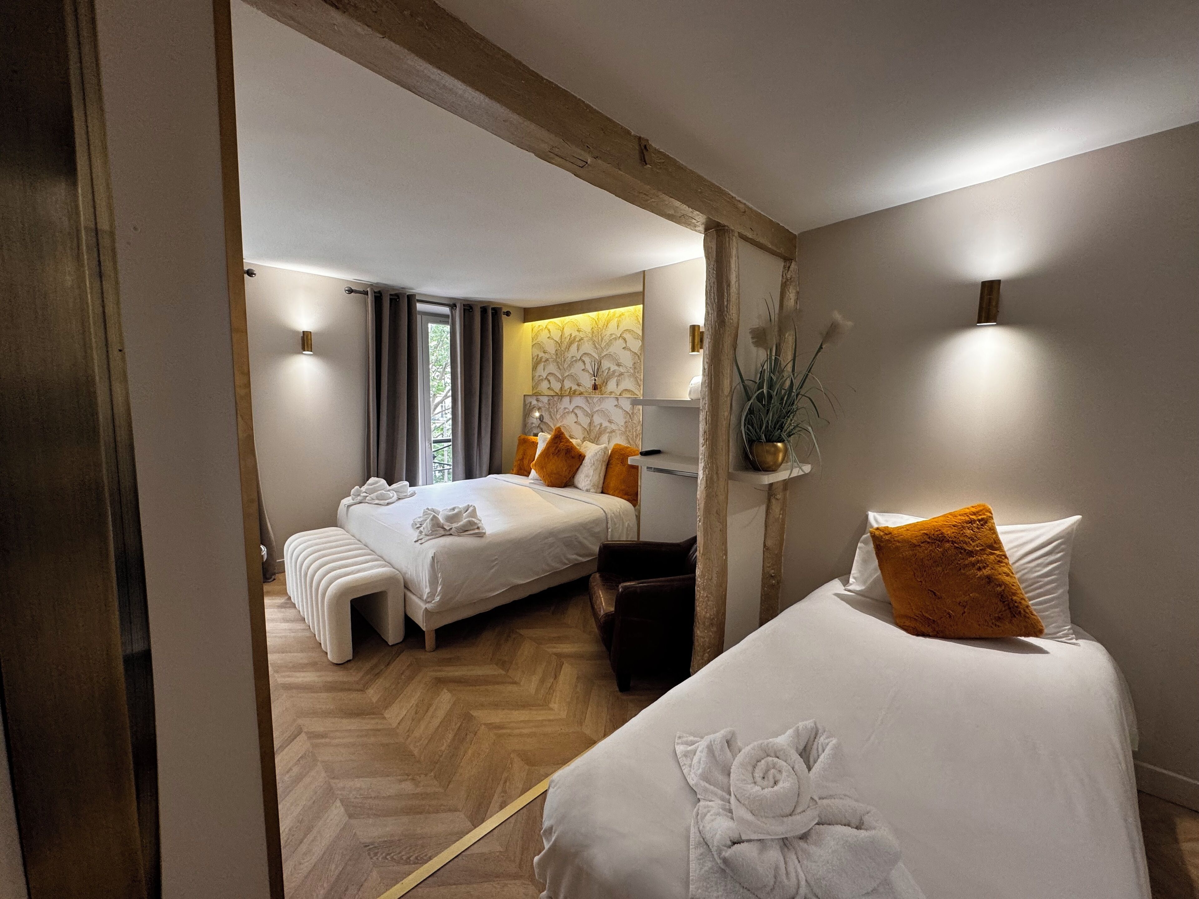 A hotel room with two beds, a wooden floor, a mirror, and a plant on a shelf.