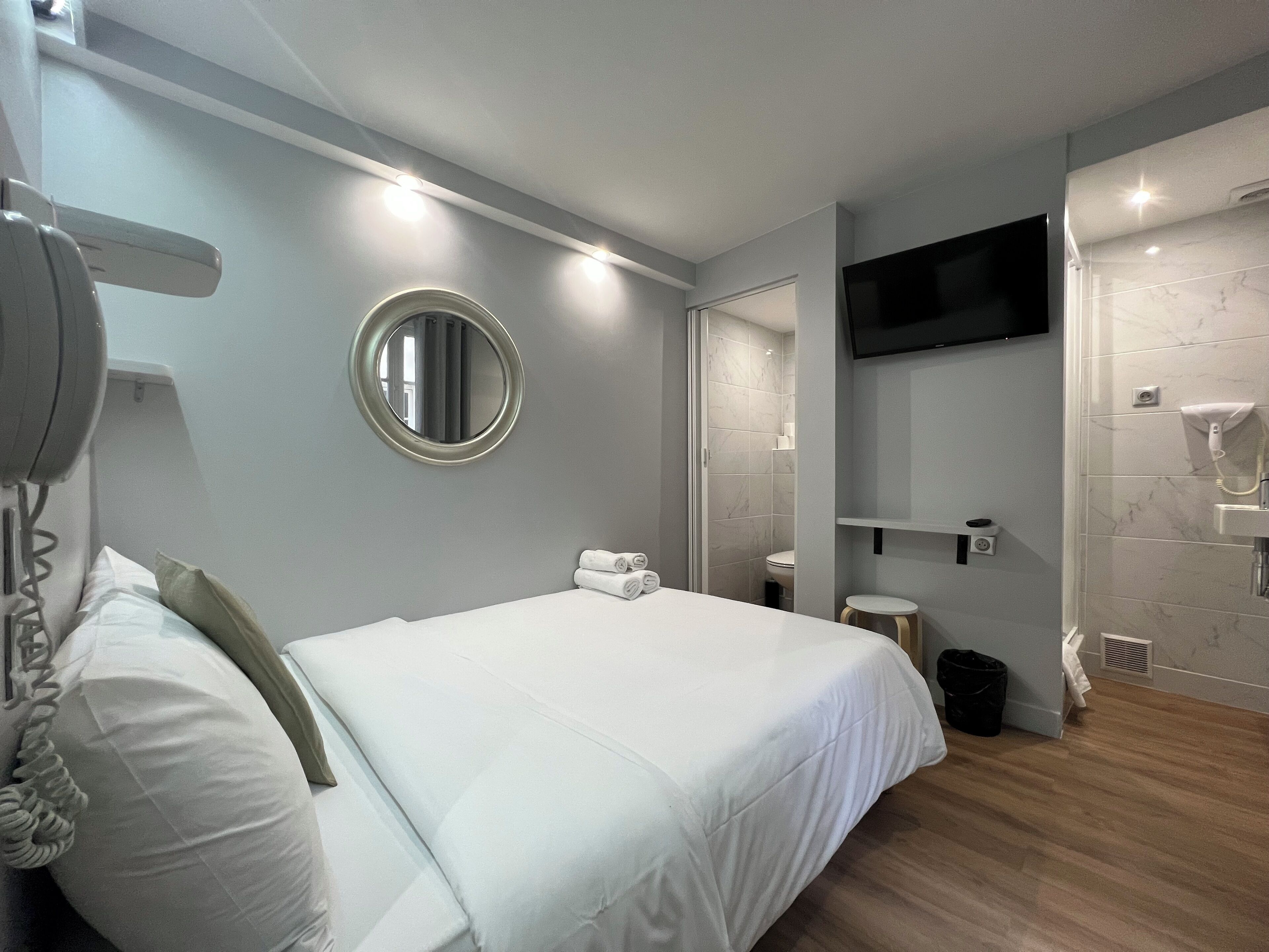 Quarto de hotel moderno com uma cama grande, um espelho redondo, televisão montada na parede e área de duche.
