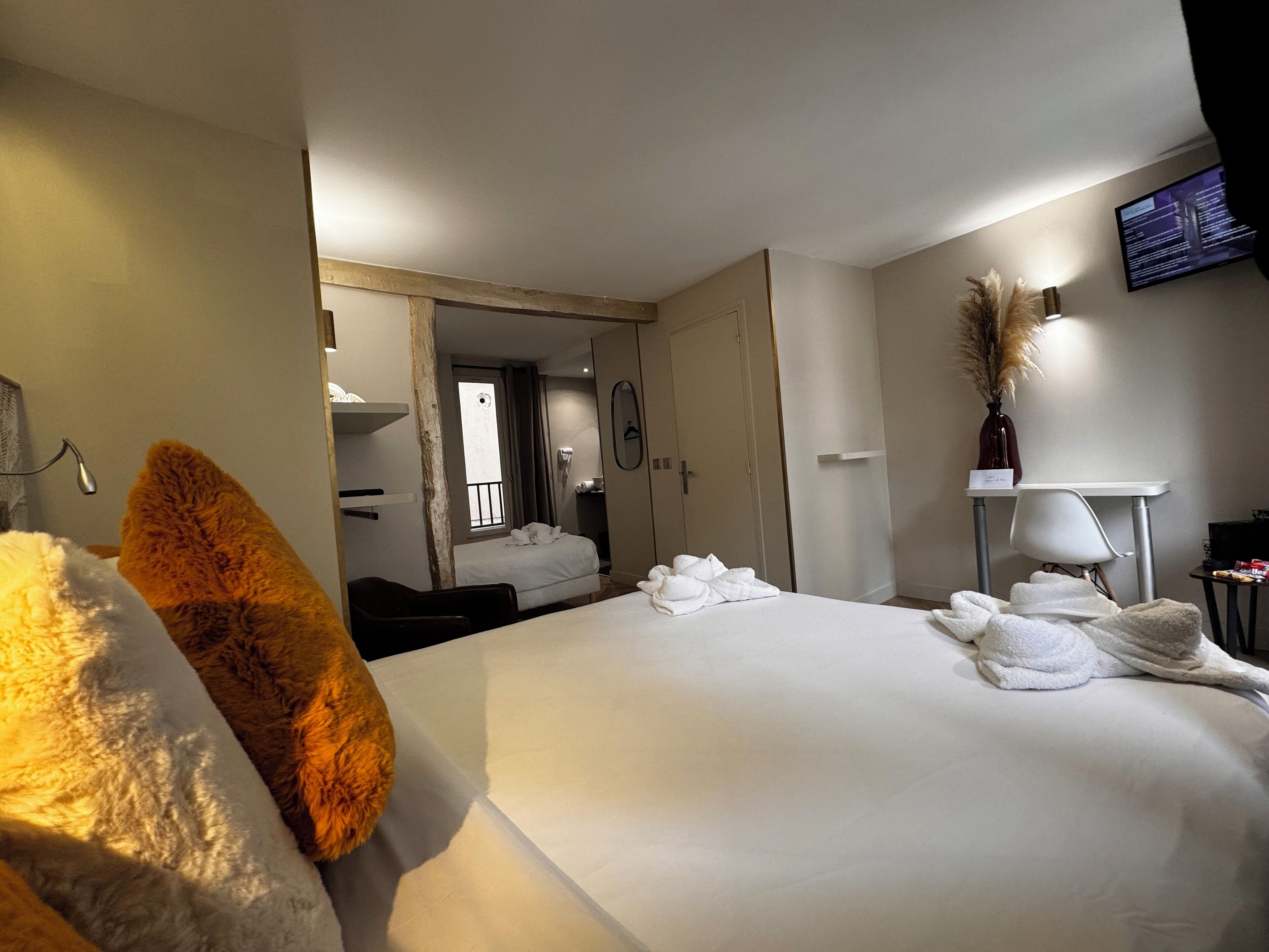 A hotel room with a large bed, a desk, a chair, a TV, and a bathroom visible through an open door.