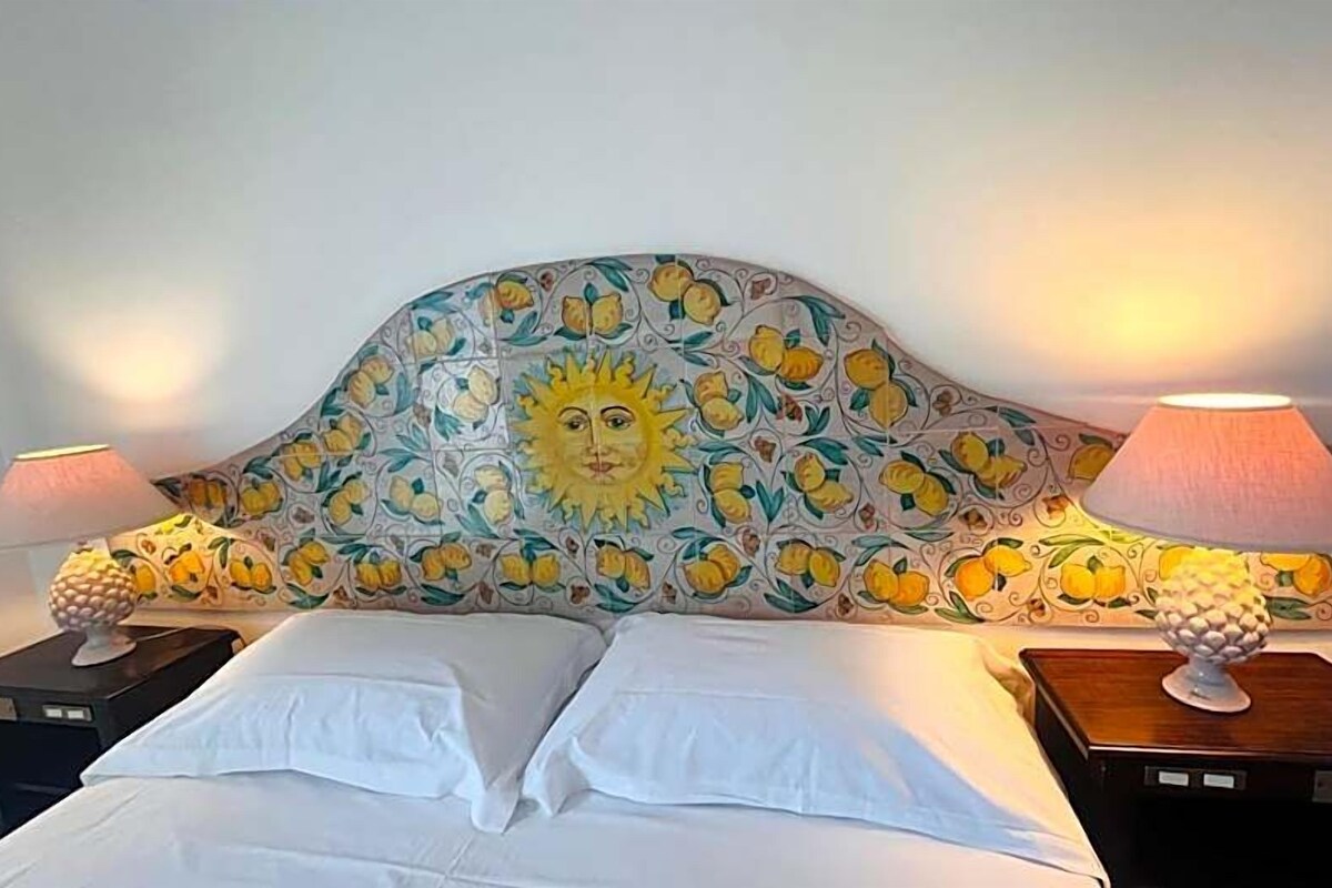 A bed with white linens, a headboard with a sun and floral pattern, and two bedside lamps on wooden nightstands.